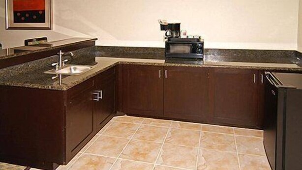 A kitchen with dark wooden cabinets, a granite countertop, a sink, and a microwave. - Fairfield Inn & Suites Hillsboro (Hillsboro)