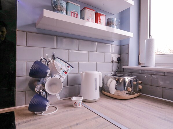 A kitchen with white tiles, a kettle, a toaster, and various mugs on the counter. - The Upper Circle (Clacton-on-Sea)