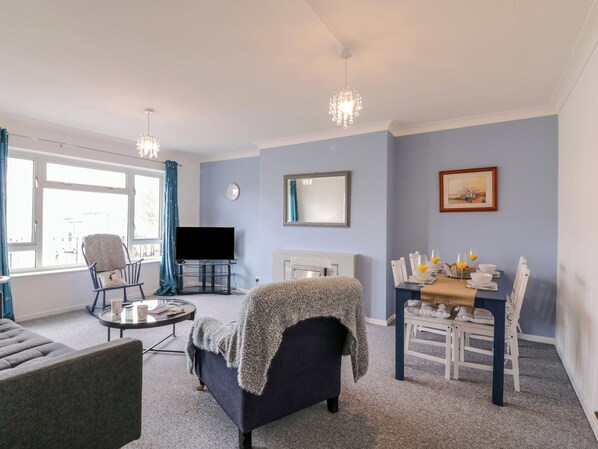 A living room with a sofa, armchair, TV, and dining table with chairs. - The Upper Circle (Clacton-on-Sea)