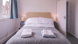 Une chambre à coucher avec un lit, deux tables de chevet avec des lampes, une fenêtre avec des rideaux et une porte.
