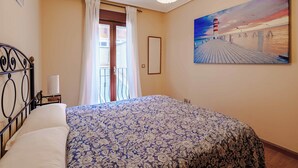 Un dormitorio con cama, mesita de noche, un cuadro y vistas al exterior.