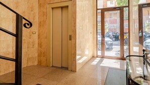Un vestíbulo de hotel con piso de mármol, un ascensor cerrado y una puerta de vidrio que da al exterior.