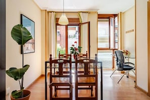Uma área de refeições com uma mesa e cadeiras de madeira, um lustre e vista para o exterior.