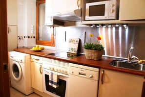 A compact kitchen with a washing machine, oven, microwave, and a sink with a stainless steel faucet.