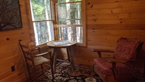 Interior acogedor de una cabaña con piso de madera, una mesa redonda con un mapa, dos sillas de madera y un tapete estampado.