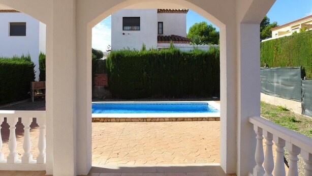 A covered outdoor area with a pool, white walls, and a view of a building with a tiled roof. - Villa California (Salou)