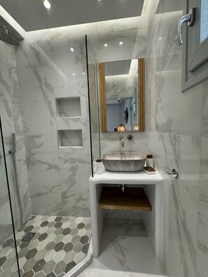 A modern bathroom with a marble vanity, a large mirror, and a shower area with hexagonal tiles. - Sunshine Bay Suites (Naxos)