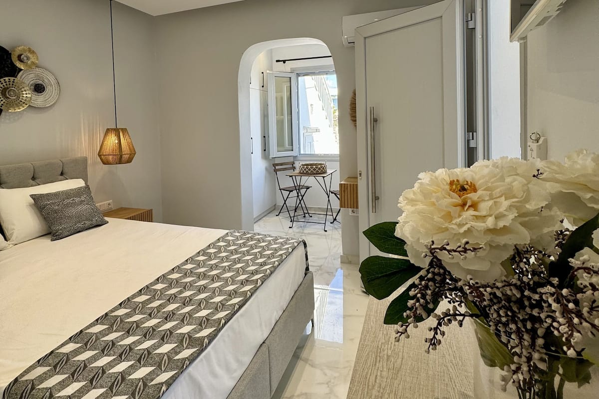 Une chambre moderne avec un grand lit, une table de chevet, une lampe suspendue et une vue sur l’extérieur.