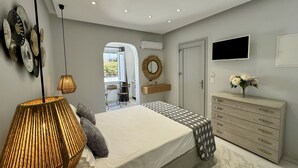 A modern bedroom with a bed, bedside lamps, a dresser, and a TV. - Sunshine Bay Suites (Naxos)