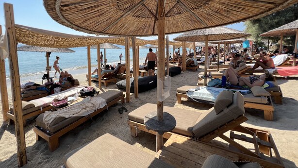 A beach with wooden lounge chairs and thatched umbrellas. - Sunshine Bay Suites (Naxos)