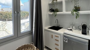 A compact kitchen with a built-in sink, a small dishwasher, and a window with curtains. - Sunshine Bay Suites (Naxos)