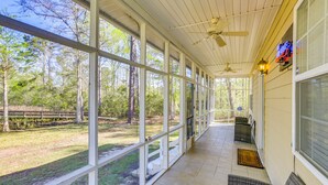 A covered porch with large windows, a ceiling fan, and a view of the surrounding trees. - Lake Seminole Retreat w/ Private Dock (Bainbridge)