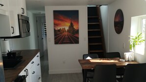 A modern kitchen with white cabinets and a wooden countertop, a dining area with a wooden table and chairs, and a staircase leading to an upper level. - Luxury Caboose in Rhododendron Forest (Agassiz)