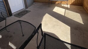 Een overdekt terras met een plafondventilator, een metalen tafel en een metalen stoel.