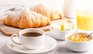 Ein Frühstückstisch mit Croissants, Butter, Orangensaft und Kaffee.