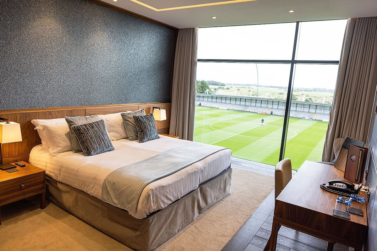 A hotel room with a large bed, a desk, and a view of a sports field.
