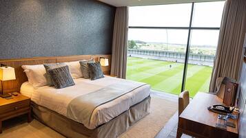 A hotel room with a large bed, a desk, and a view of a sports field.