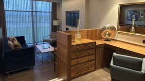A modern hotel room with a wooden desk, a comfortable sofa, a TV, and a large window with curtains. - The Hotel at Mill Farm (Preston)