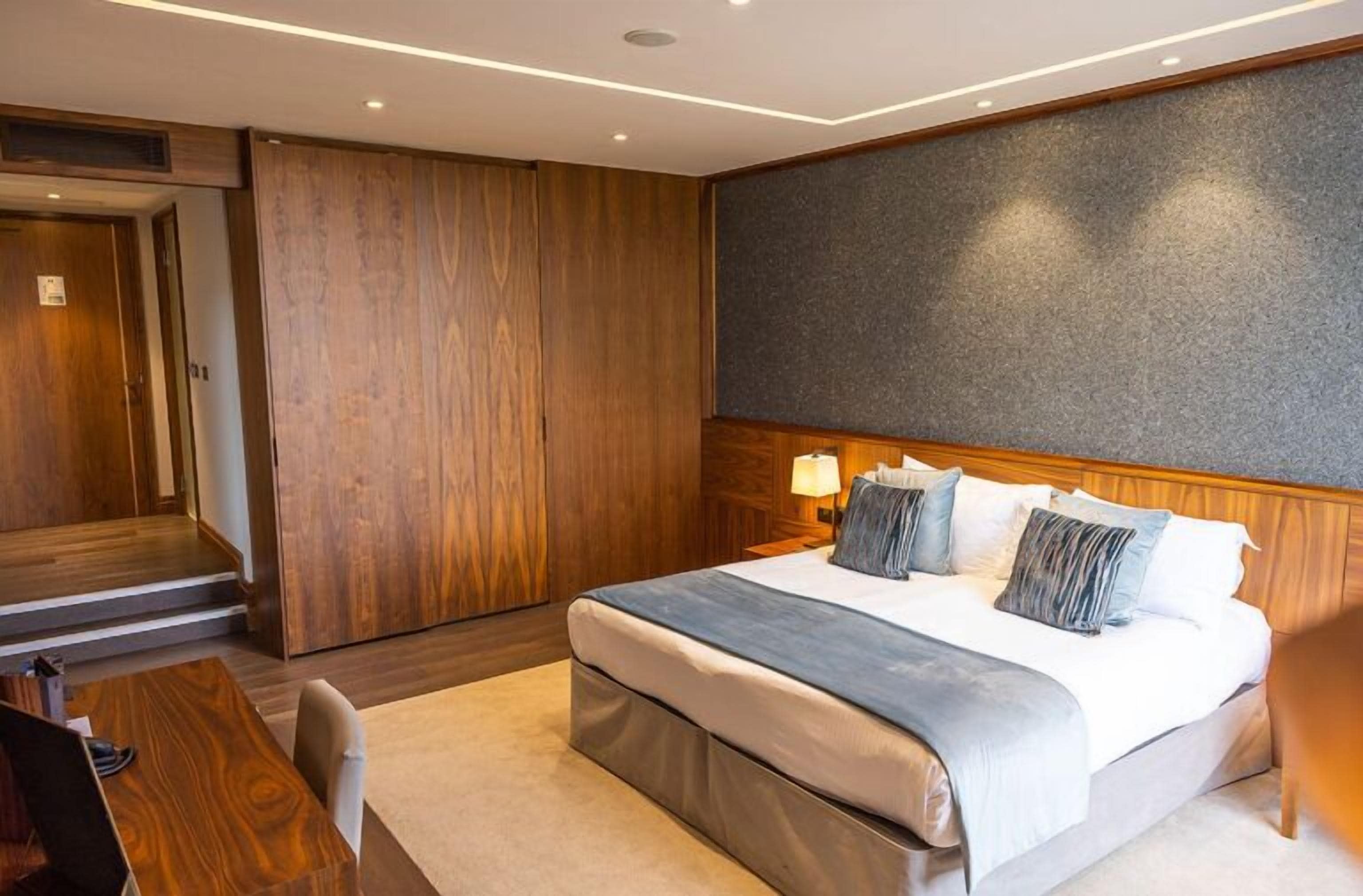 A modern hotel room with a large bed, wooden paneling, a desk, and a seating area.