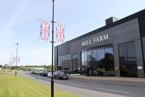 Ein modernes Gebäude mit dem Schild "MILL FARM" auf der Fassade, mit großen Fenstern und einem Parkplatz mit Autos.