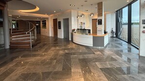 A spacious lobby with a curved reception desk, a staircase, and a large window offering a view. - The Hotel at Mill Farm (Preston)