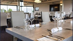 A dining table set with wine glasses, cutlery, and a folded napkin, with a modern interior and large windows in the background. - The Hotel at Mill Farm (Preston)