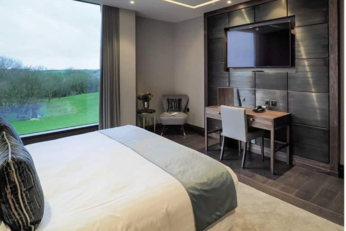 A modern hotel room with a large bed, a desk, and a TV mounted on the wall.