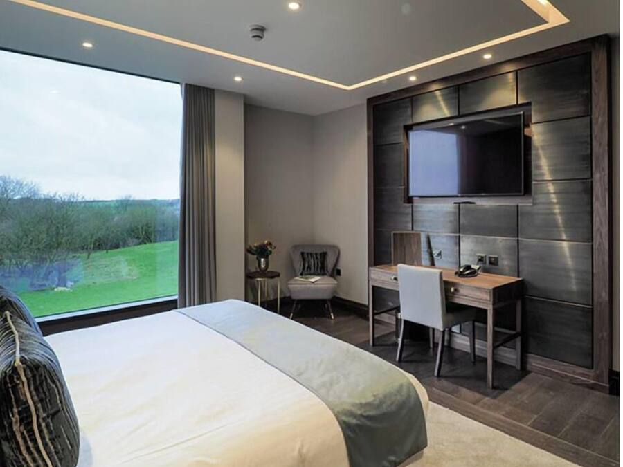 A modern hotel room with a large bed, a desk, and a TV mounted on the wall.