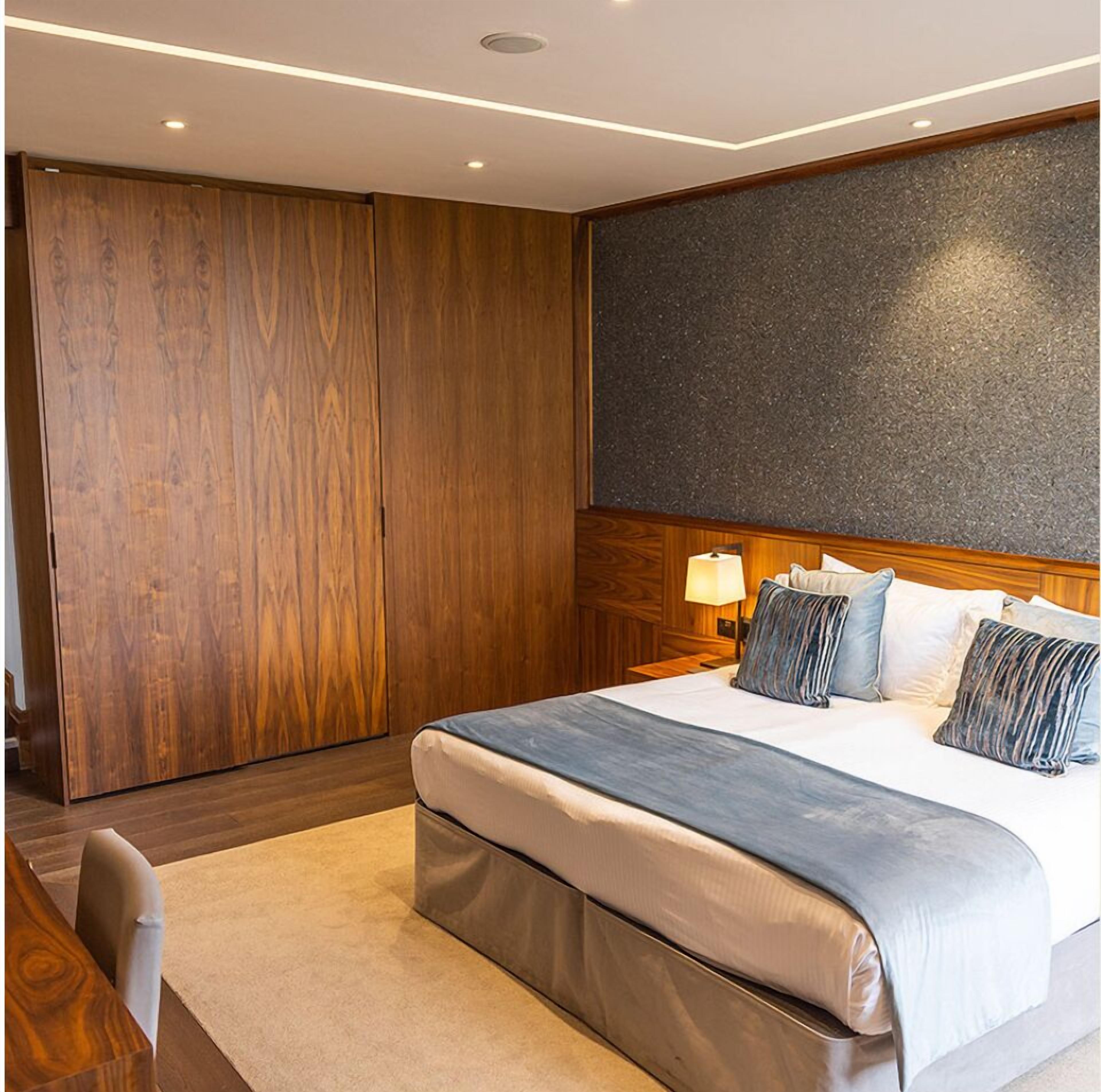 A modern hotel room with a large bed, wooden wardrobe, and a dark textured wall.