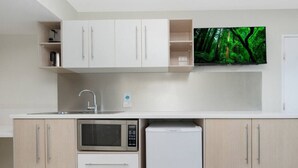 A modern kitchen with white cabinets, a microwave, a refrigerator, a sink, and a flat-screen TV mounted above the counter.