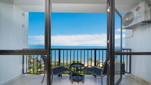 A balcony with a view of the sea, a table, and two chairs.