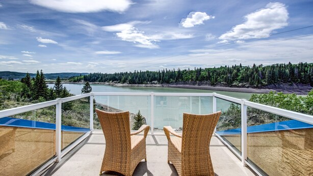 A balcony with wicker chairs overlooking a lake and forest. - Unique Cottage (Ghost Lake)