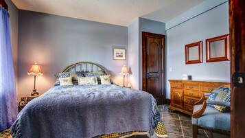 A bedroom with a bed, two bedside lamps, a wooden dresser, a chair, and a door.