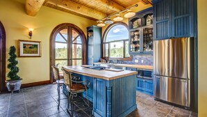 A kitchen with a central island, wooden ceiling, and large windows. - Unique Cottage (Ghost Lake)