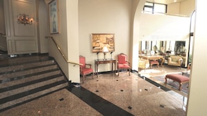 Un vaste hall d’entrée agrémenté d’un escalier en marbre, d’un lustre et d’un espace salon avec une table et des chaises.
