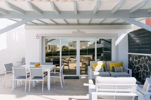 An outdoor patio with white furniture, a glass door leading to a view of buildings, and a stone wall.