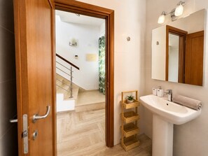 A bathroom with a wooden door, a white sink, a mirror, and a staircase leading to another room.