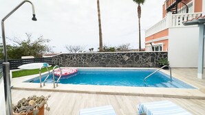 A swimming pool with a stone wall, lounge chairs, and a palm tree.