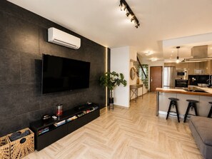 A modern living room with a flat-screen TV, a black entertainment unit, and a wooden herringbone floor.