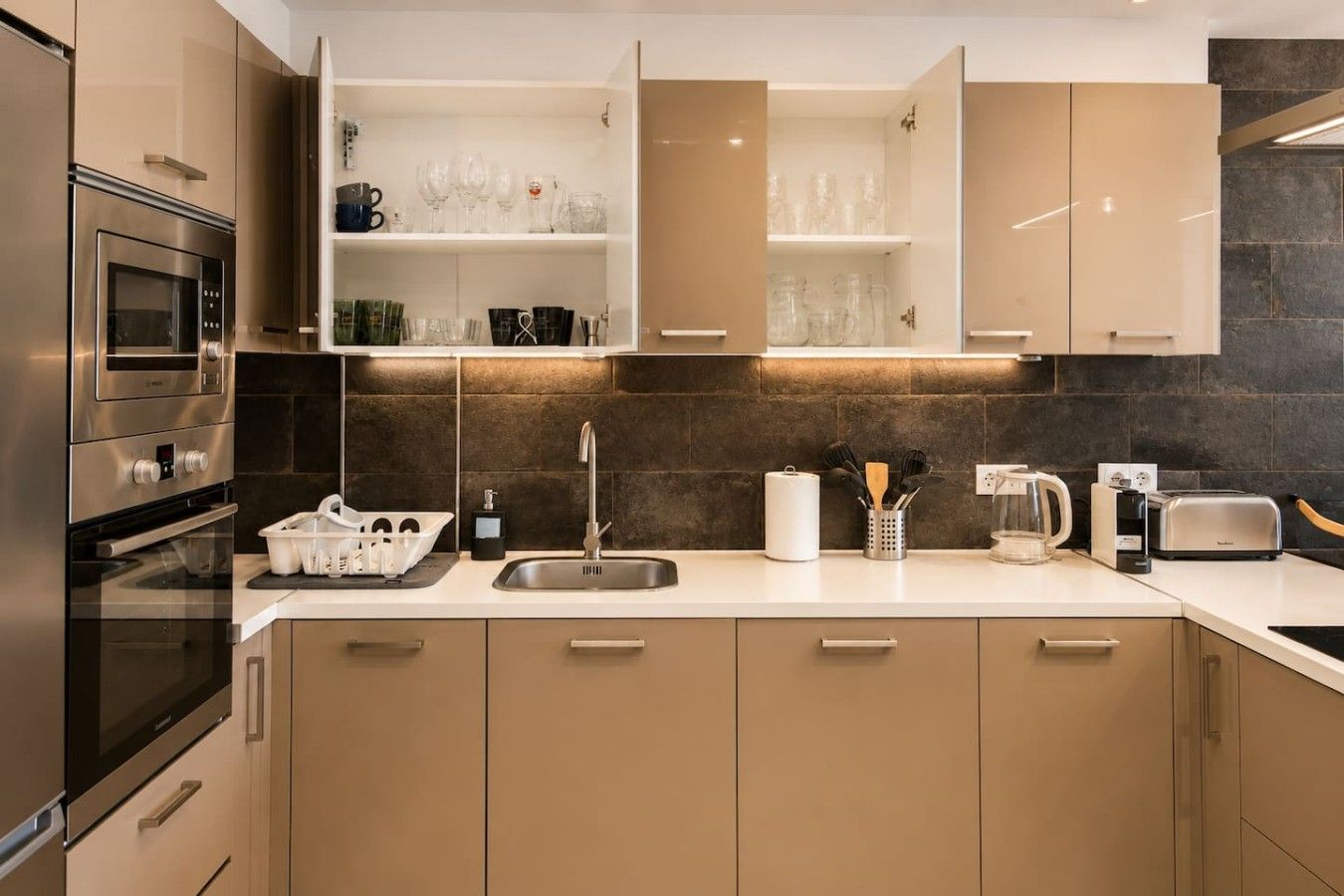 A modern kitchen with built-in appliances, a sink, and open shelving with glassware.