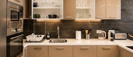 A modern kitchen with built-in appliances, a sink, and open shelving with glassware.