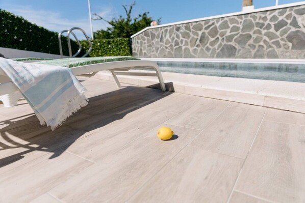 A poolside area with a lounge chair, a stone wall, and a yellow ball on the floor.