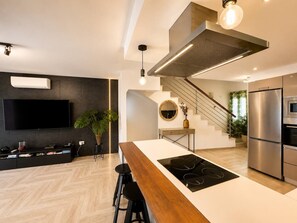 Een moderne keuken met een centraal kookeiland, roestvrijstalen apparatuur en een trap naar een verdieping erboven.