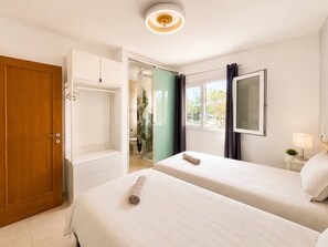 Une chambre d’hôtel avec deux lits, une armoire, une salle de bain avec des toilettes et un lavabo, et une fenêtre avec des rideaux.