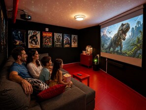 A family watching a movie on a large screen in a cozy room with a red floor, a popcorn bucket, and movie posters on the wall.