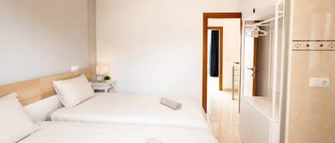 A hotel room with two beds, a bathroom, and a nightstand with a lamp.