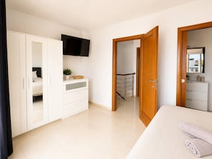 Ein Schlafzimmer mit Bett, Kleiderschrank, Fernseher und angrenzendem Badezimmer.