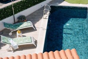 Ein Poolbereich auf dem Dach mit zwei Liegestühlen, einem kleinen Tisch mit Früchten und einer Topfpflanze.