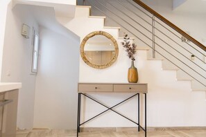 Een moderne trap met een glazen balustrade, een console tafel met een spiegel, en een vaas met bloemen.