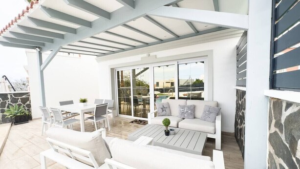 An outdoor patio area with white furniture, a coffee table, and a view of a swimming pool.
